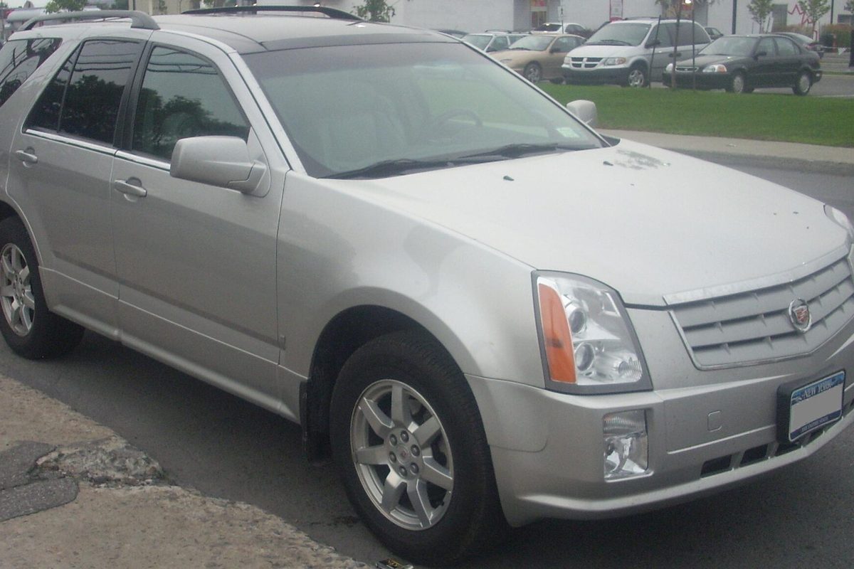 A silver first-generation Cadillac SRX crossover parked by a curb, seen from the front and driver's side