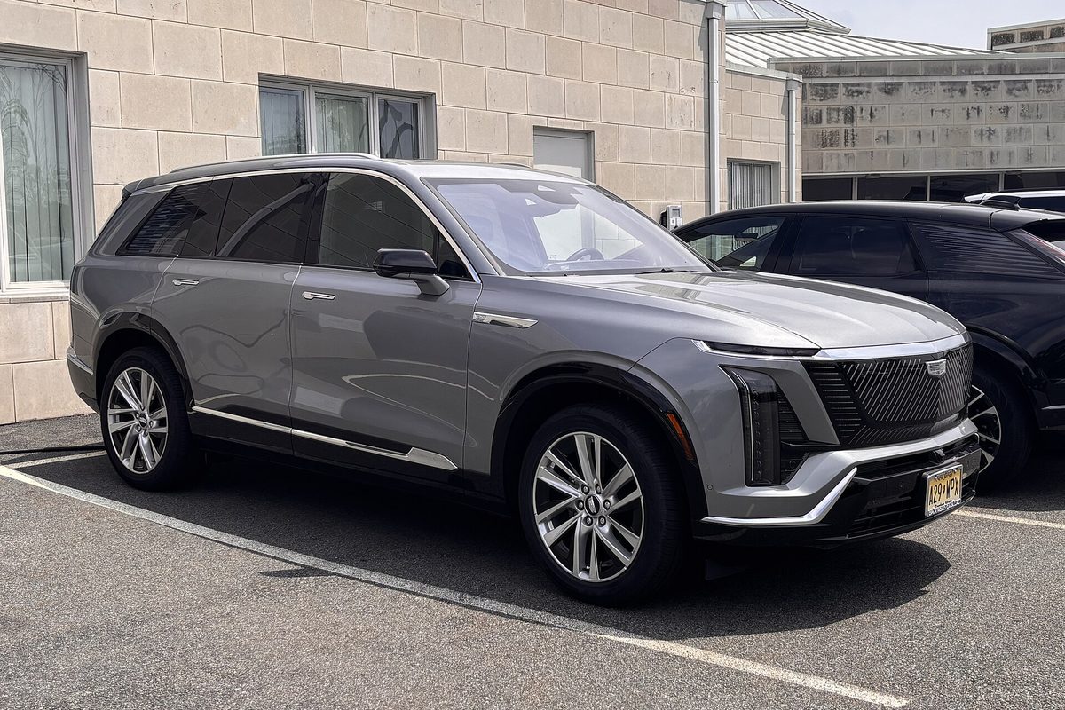 A gray Cadillac Vistiq electric SUV, front three-quarter view, parked outside a tan stone building