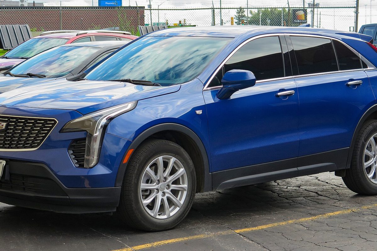A bright blue Cadillac XT4 small SUV with silver wheels, parked in a lot beside other cars, seen from the front left