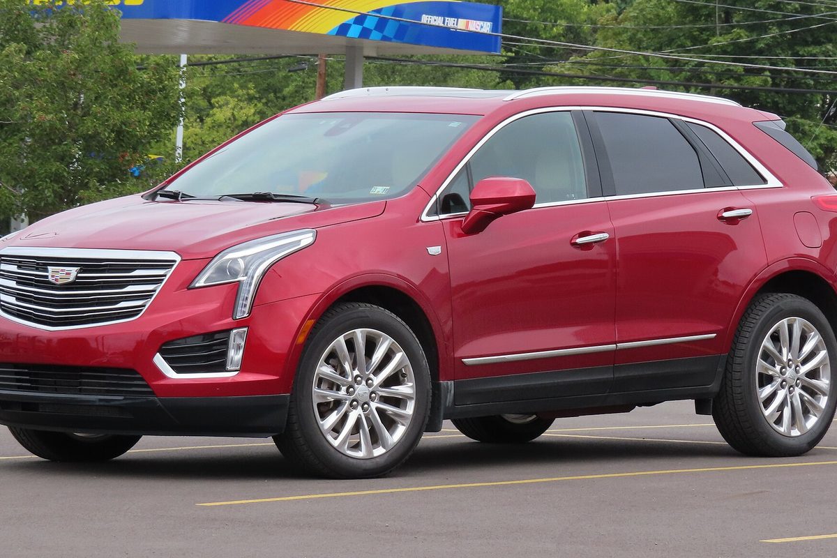 A red Cadillac XT5 crossover with silver wheels, seen from the front left in a gas station lot