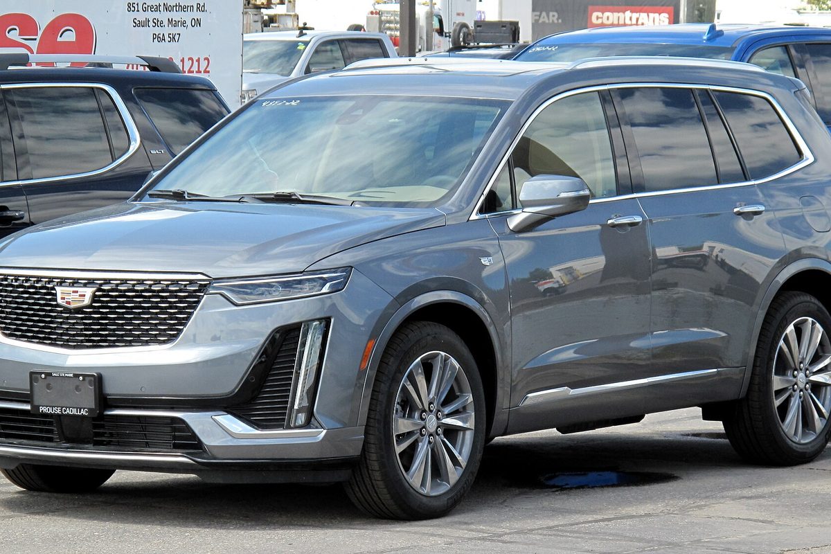 A gray Cadillac XT6 crossover with silver wheels, parked in front of a dealership sign, seen from the front left