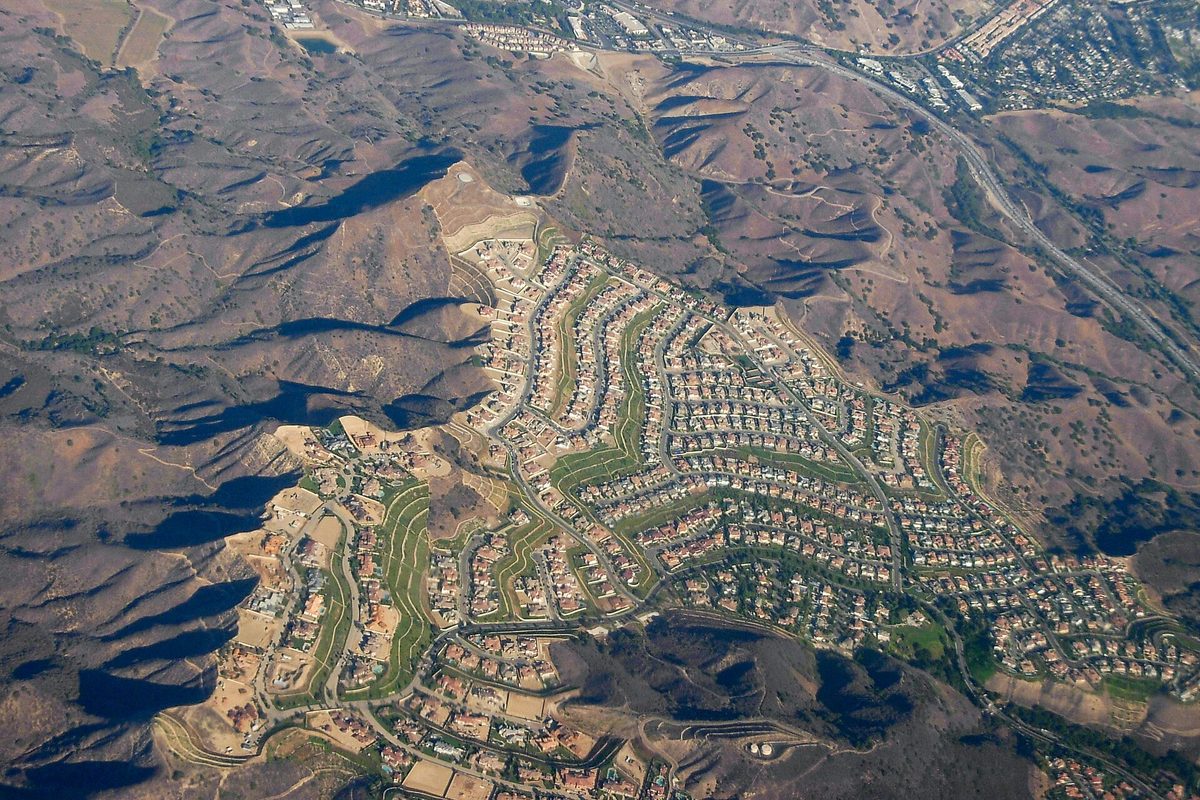 Aerial view of a Calabasas hillside neighborhood, its curving streets of houses set among dry brown hills, with U.S. Route 101 running across the upper right