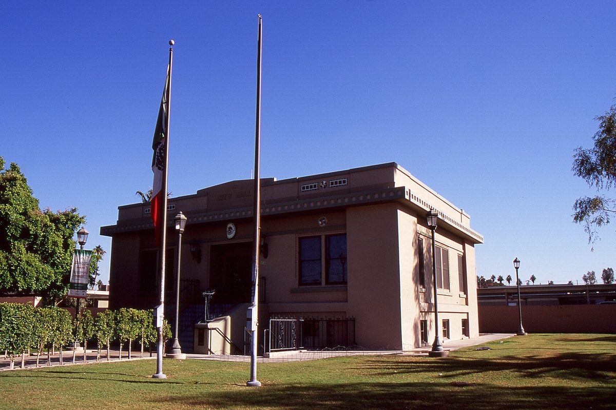 Calexico's old city hall, a tan two-story building with two flagpoles on the lawn in front, under a clear blue sky