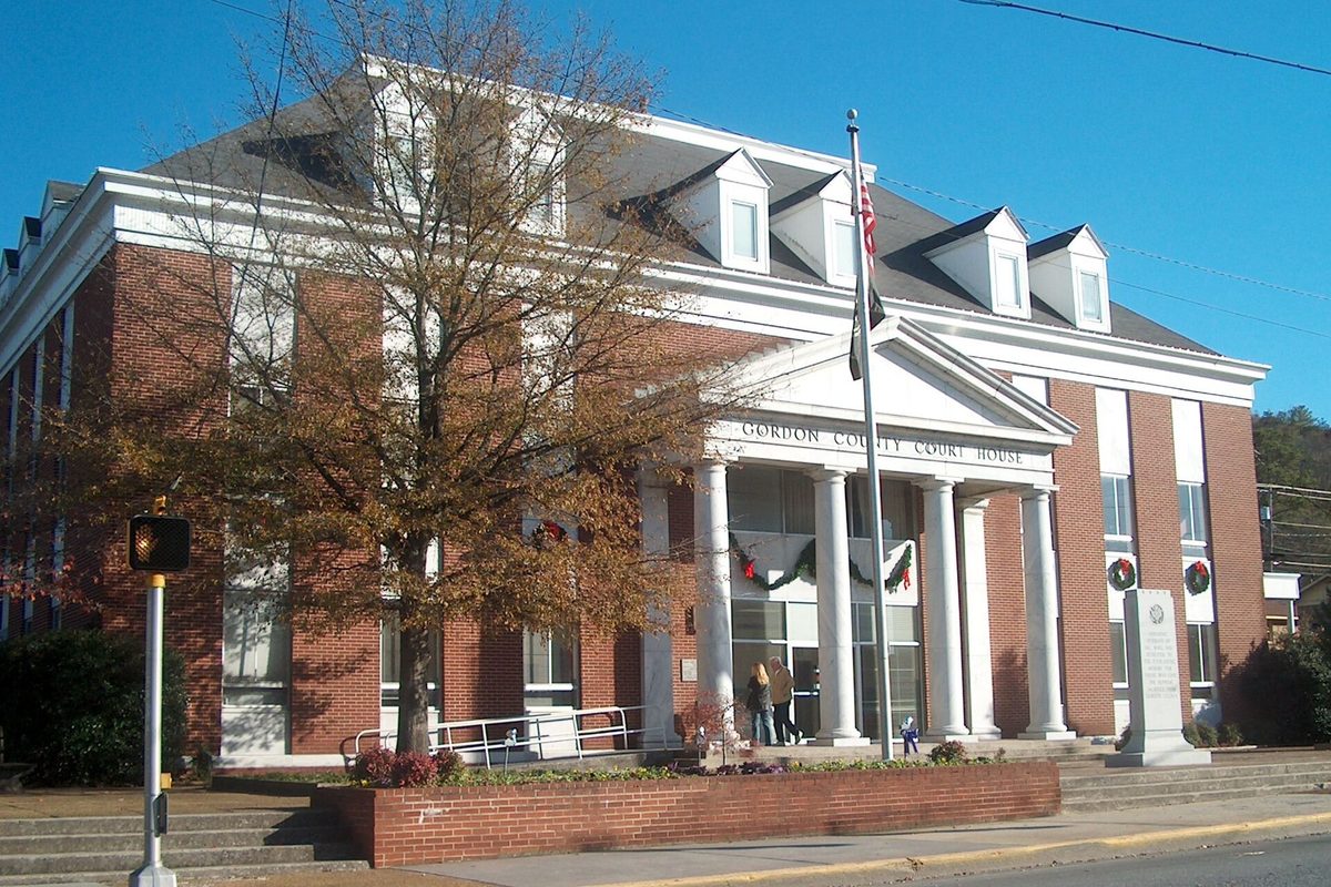 The red-brick Gordon County Court House in Calhoun, with white columns and holiday wreaths, beside a tree in fall color