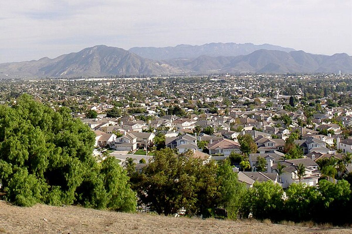 Camarillo seen from a dry hillside, rooftops and trees spreading across the valley toward a mountain range under a pale sky