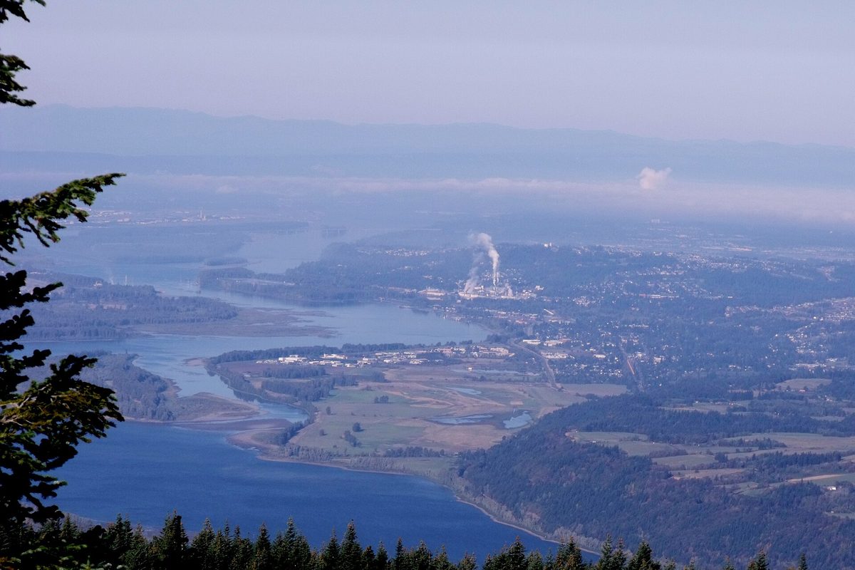 Camas and the Columbia River seen from a forested hilltop, with steam rising from an industrial plant on the riverbank
