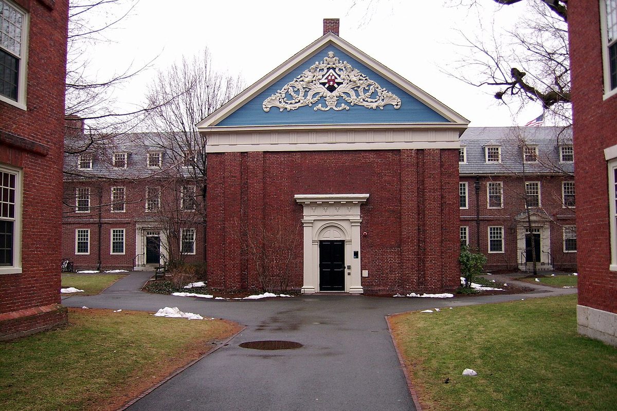 Holden Chapel in Harvard Yard, a red brick building with a blue pediment and white carved ornament, a path leading to its door and patches of snow on the grass