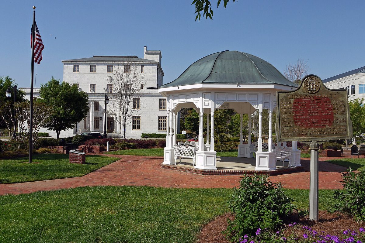 Downtown Canton's town square with a white domed gazebo, an American flag on a tall pole, a historical marker and a large white building behind brick walkways