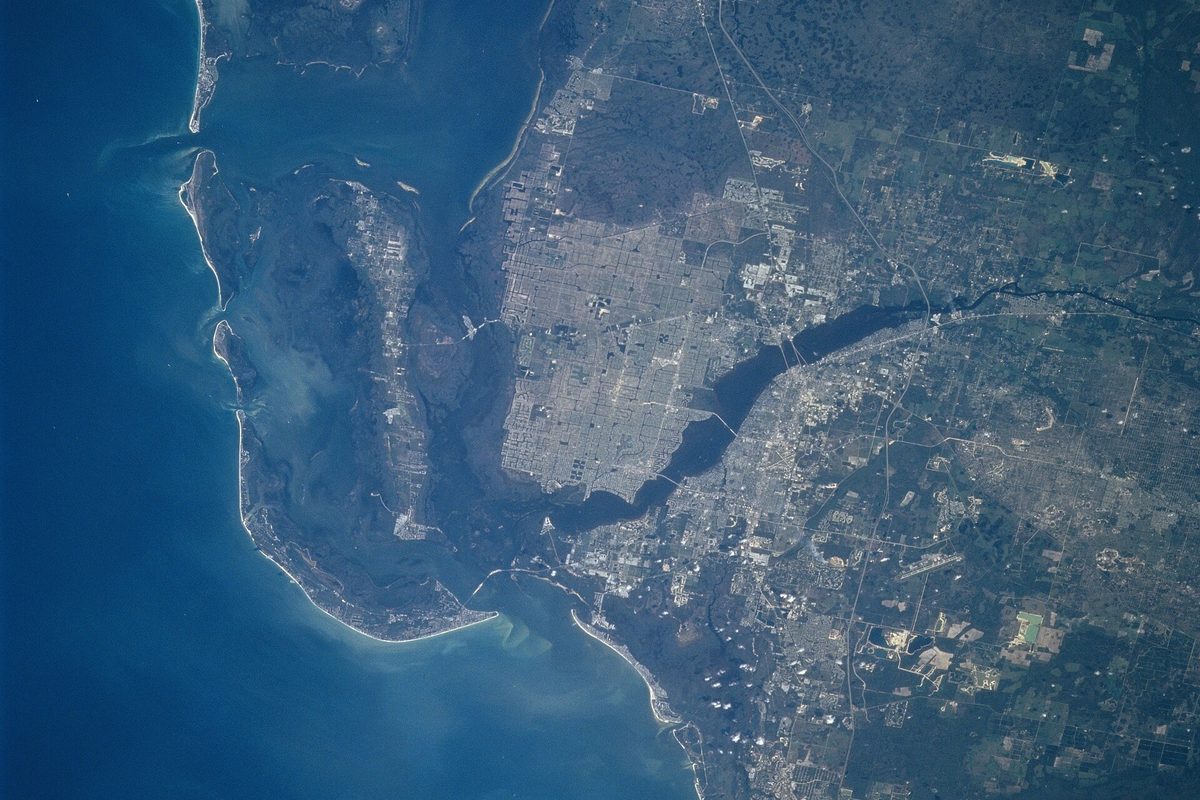 Astronaut photo of Cape Coral from orbit: the city's grid of streets and canals beside the Caloosahatchee River, with Fort Myers across the water and barrier islands along the Gulf