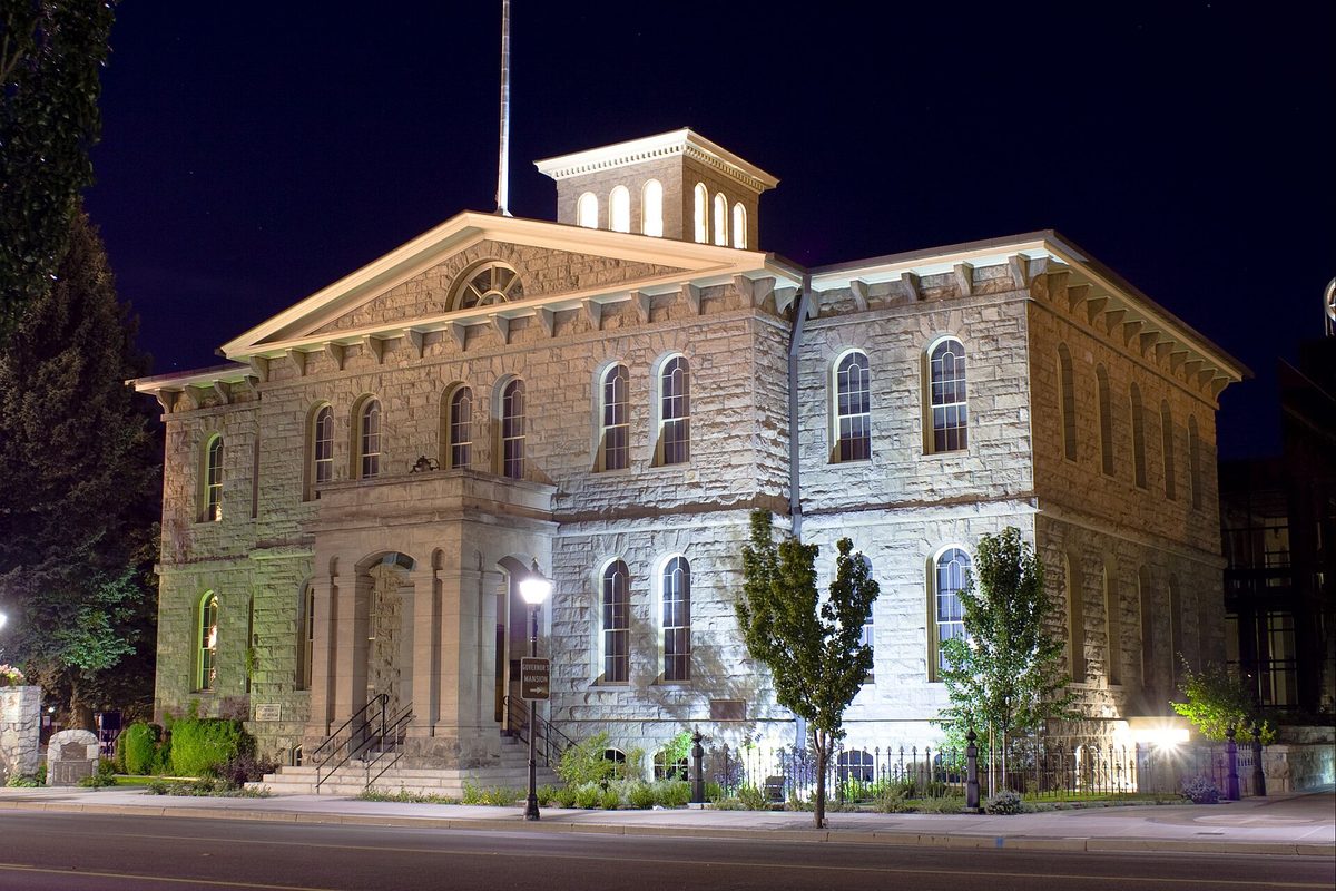The stone Nevada State Museum in Carson City lit up at night, with arched windows, a columned porch and a small cupola on the roof