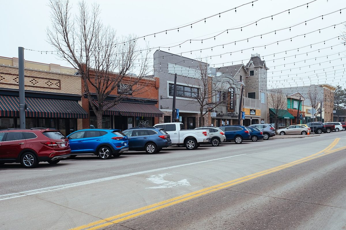 Wilcox Street in downtown Castle Rock on an overcast day, with SUVs and a pickup parked in front of shops under strings of lights