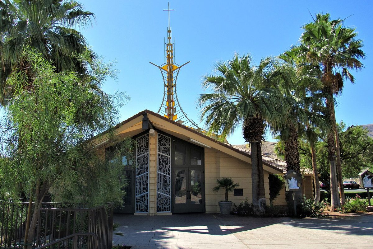 St. Louis Catholic Church in Cathedral City, a small building with lattice-patterned windows and a tall gold spire, surrounded by palm trees and desert shrubs