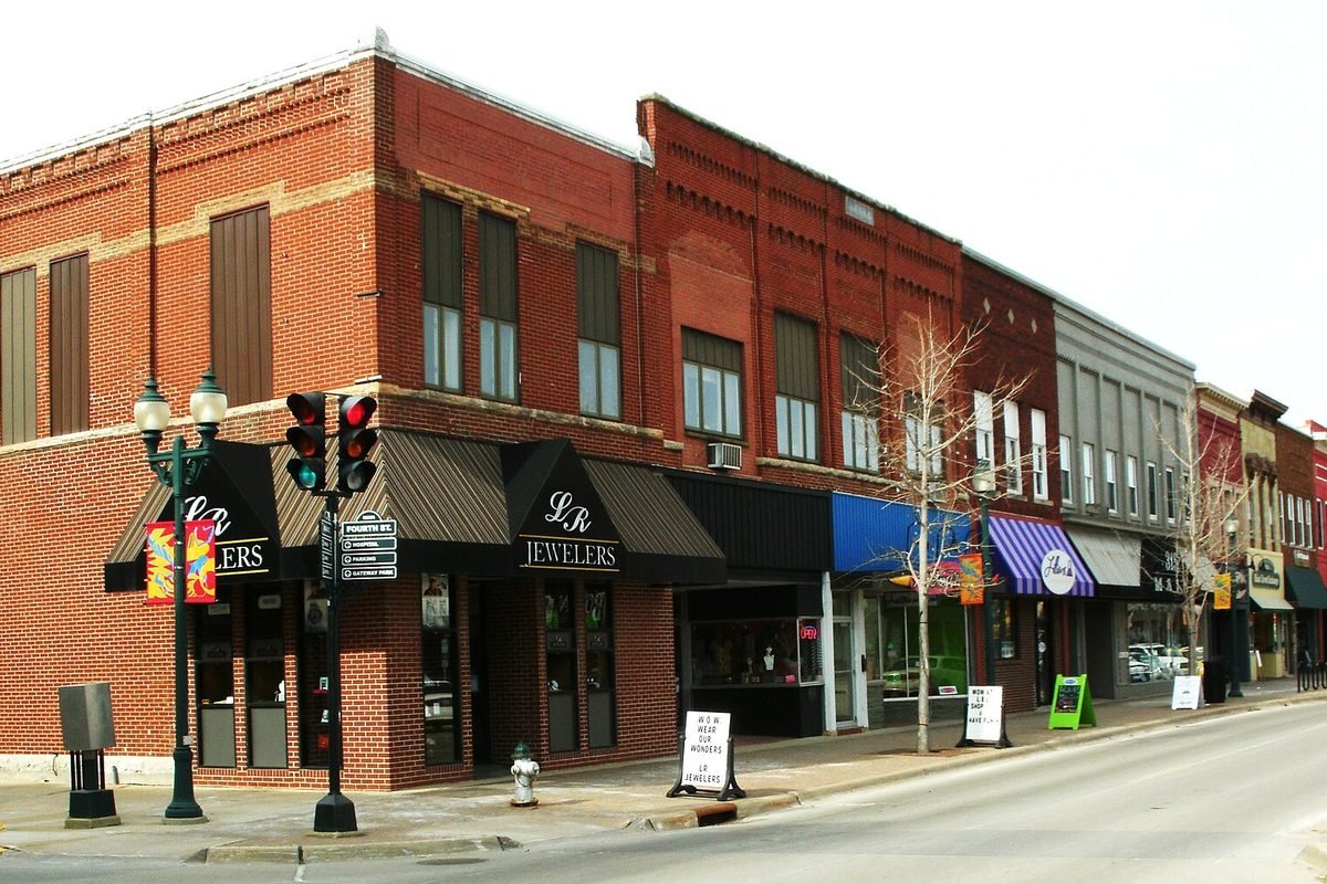 Red brick storefronts on Main Street in downtown Cedar Falls, with a jewelry store on the corner, black awnings and a traffic signal at the curb