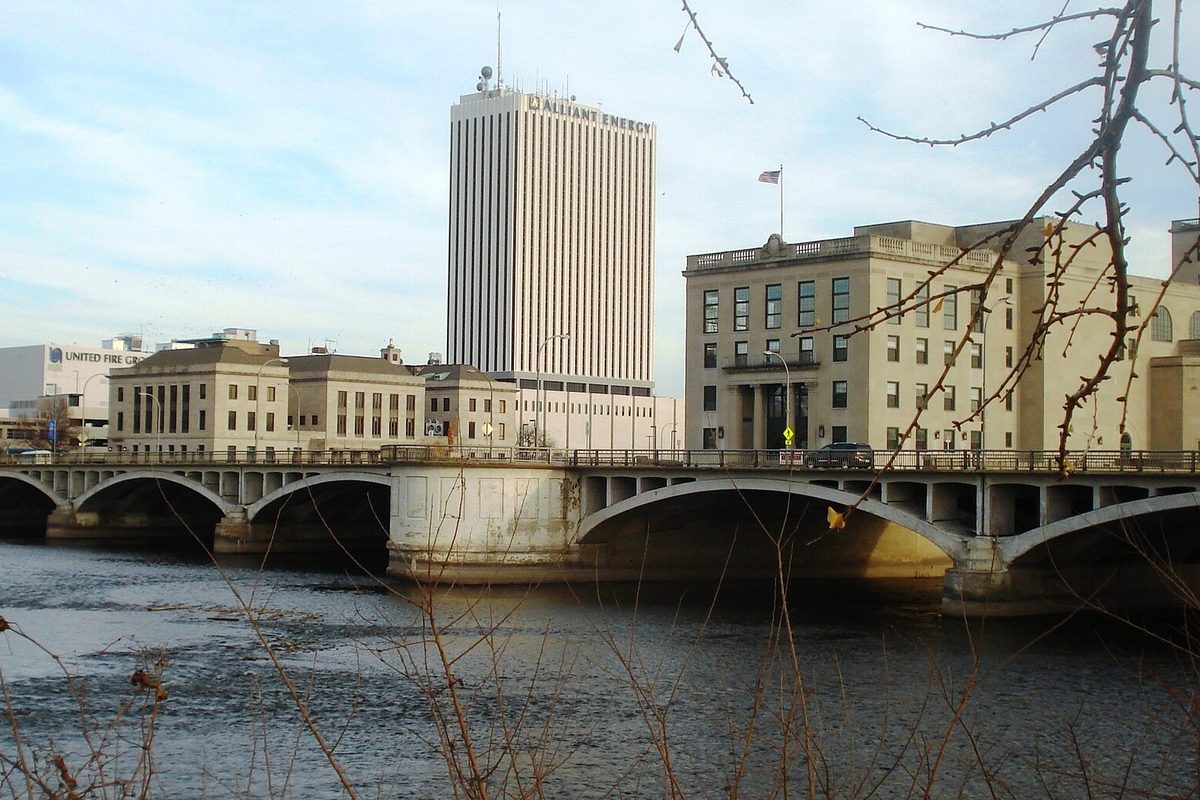 The arched concrete First Avenue Bridge over the river in downtown Cedar Rapids, with a tall white office tower and stone buildings behind it