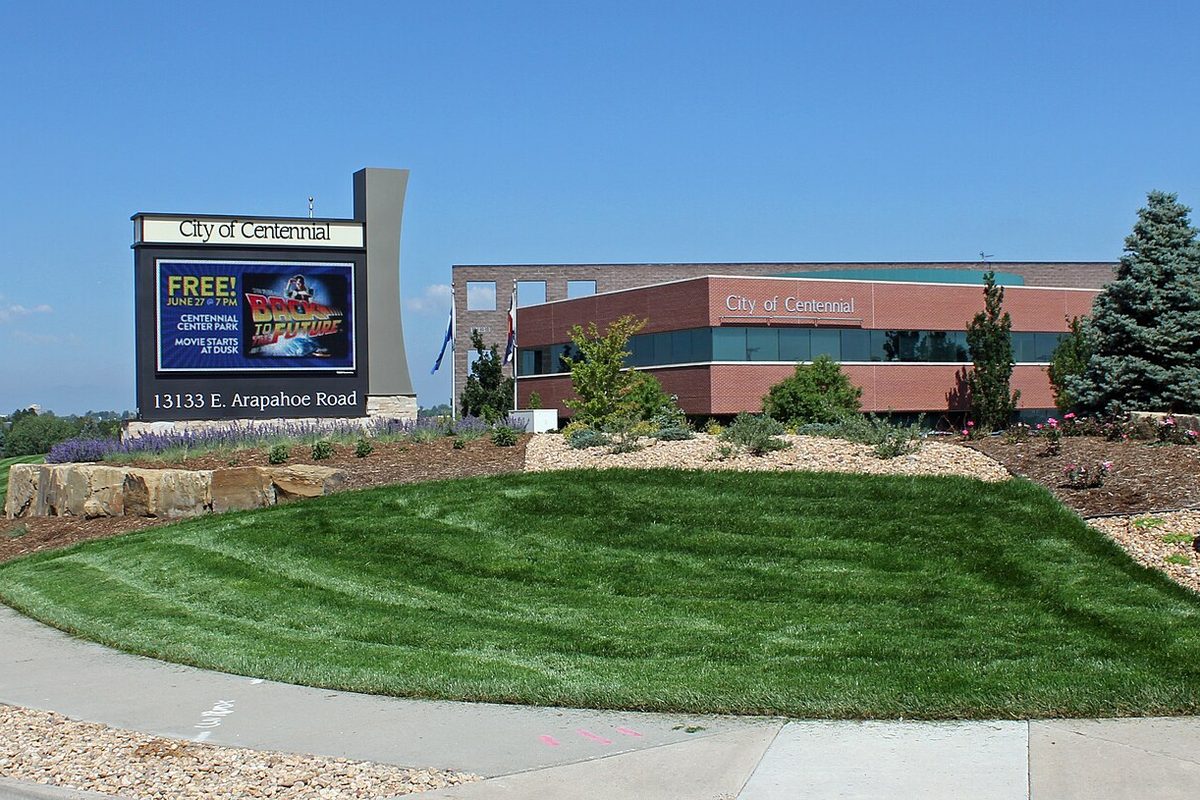 The low red brick Centennial Civic Center behind a mowed lawn, with a City of Centennial sign reading 13133 E. Arapahoe Road