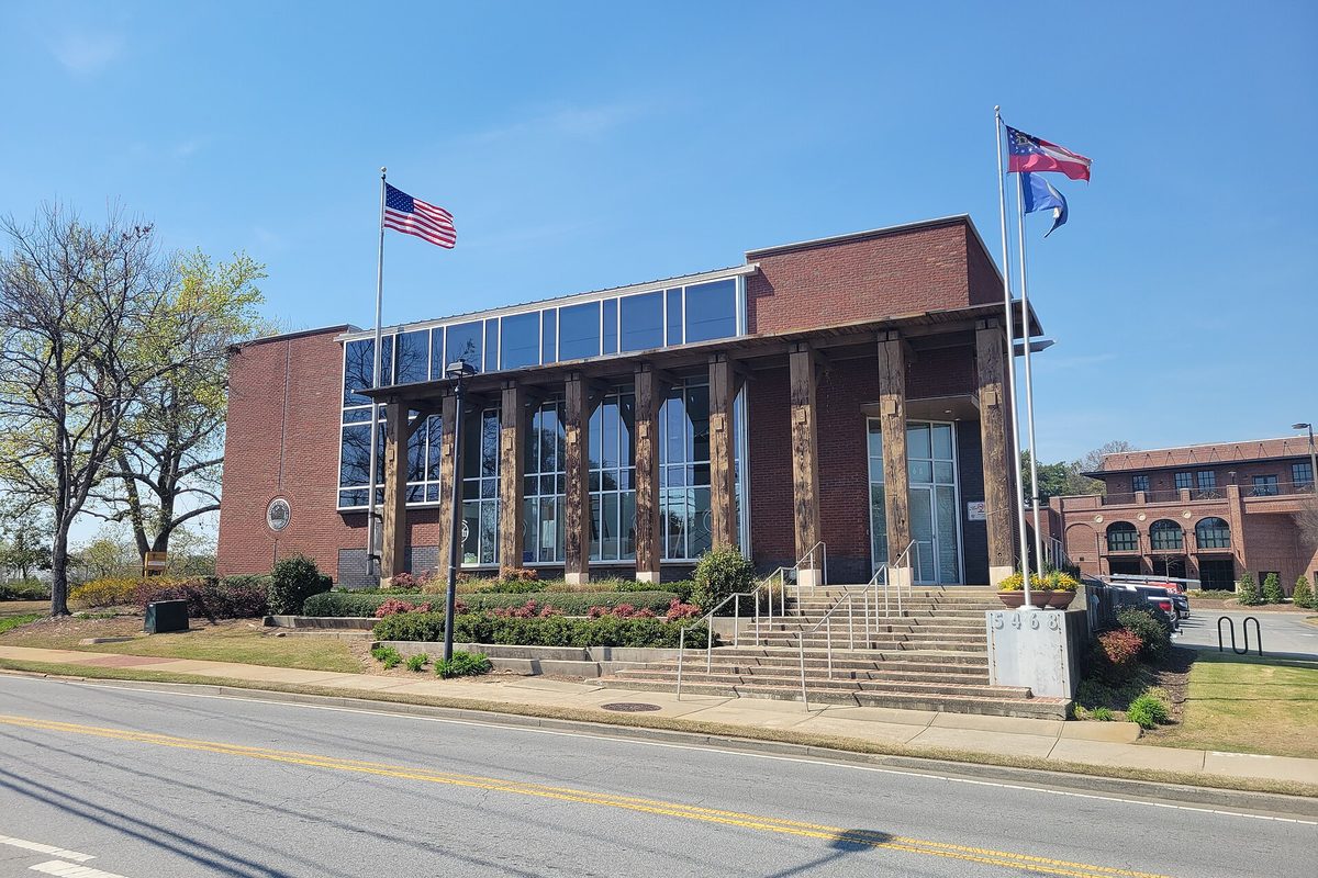 Chamblee's former City Hall, a brick and glass building with heavy timber columns, wide front steps and flags flying on a clear spring day