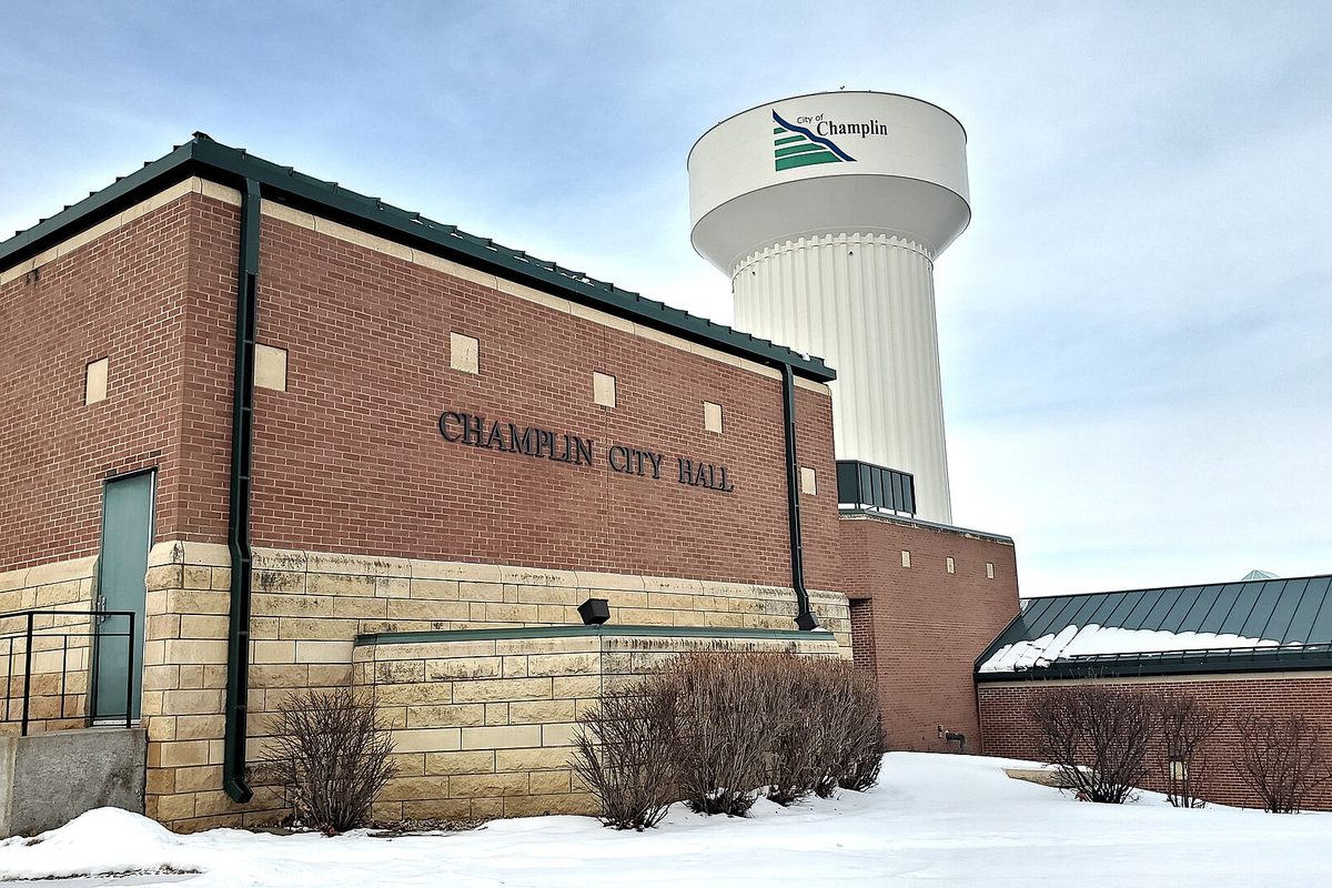 Champlin City Hall's brick and stone wall with its name in metal letters, the white Champlin water tower behind it and snow on the ground