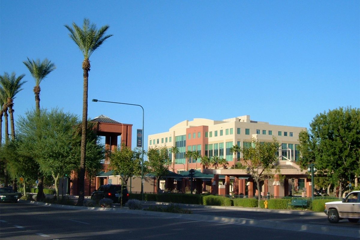 A tan and coral office building with green glass behind tall palm trees on a sunny downtown Chandler street
