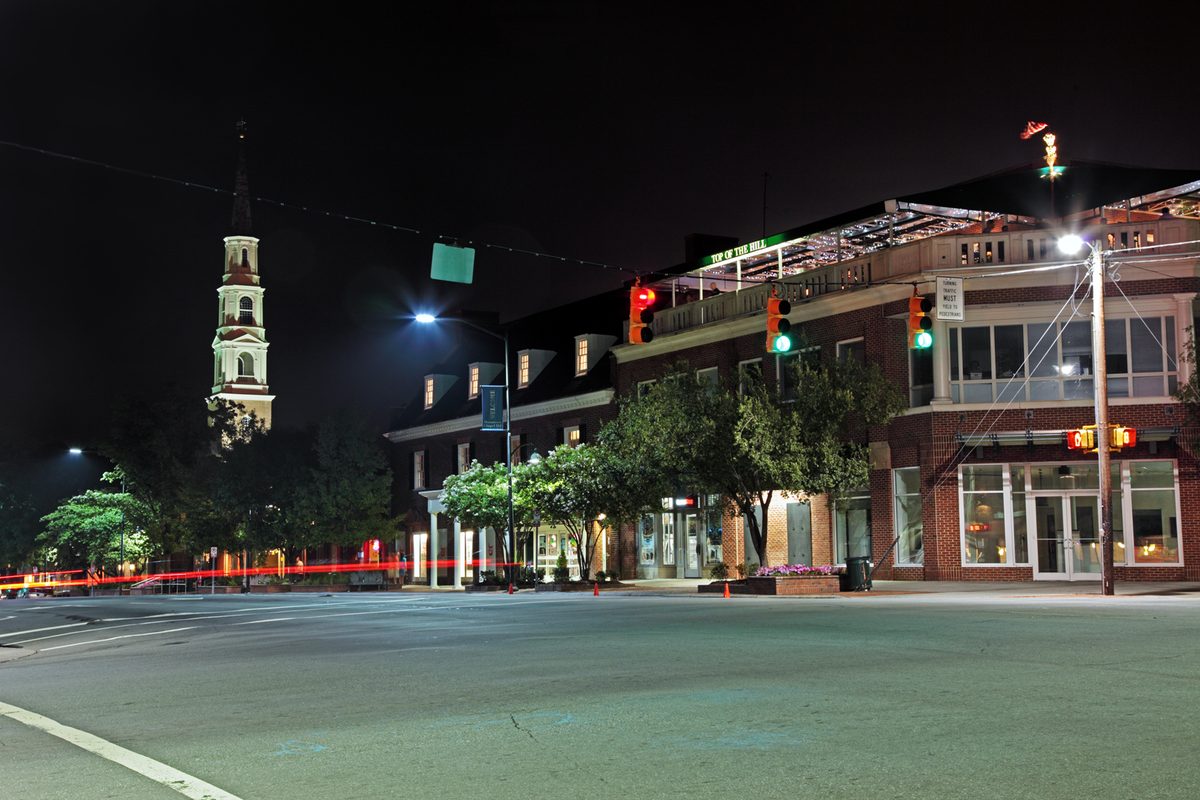 Franklin Street at Columbia Street in Chapel Hill at night, brick storefronts under street lamps and a white church steeple on the left