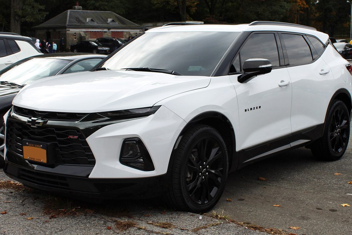 A white 2020 Chevrolet Blazer RS crossover with black wheels and a black grille, parked on leaf-strewn pavement beside a park building