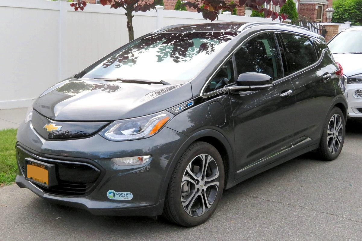 A dark gray 2017 Chevrolet Bolt EV Premier hatchback at a residential curb in front of a white fence, with a Clean Pass decal on its bumper