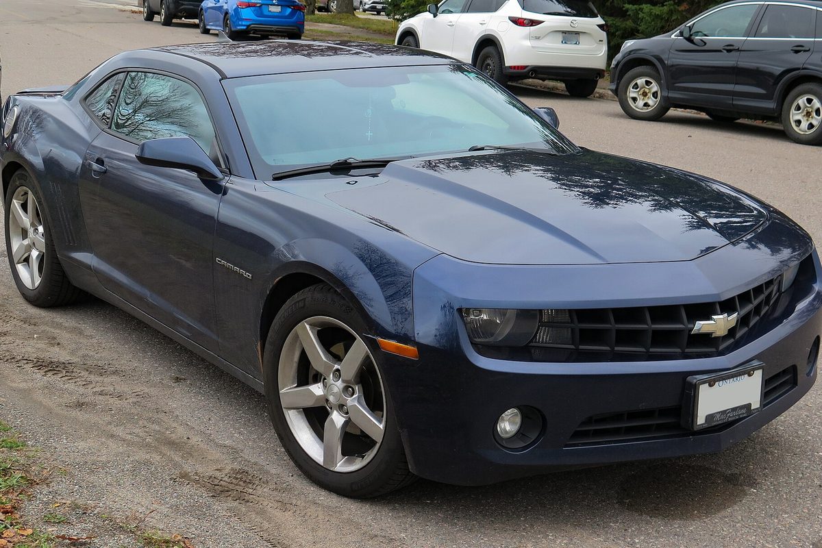 A dark blue 2012 Chevrolet Camaro 1LT coupe parked on sandy ground beside a road, seen from the front right
