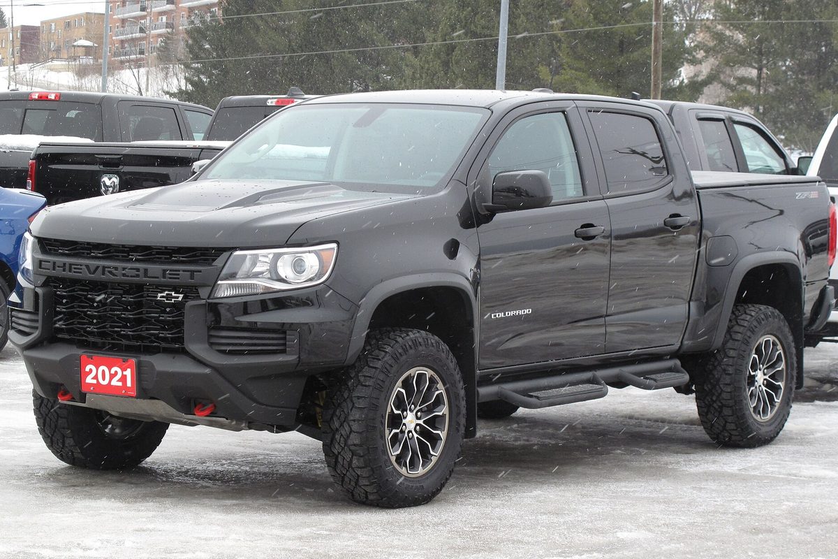 A black 2021 Chevrolet Colorado ZR2 crew cab on off-road tires, parked on a snowy dealer lot with a 2021 sign on the bumper