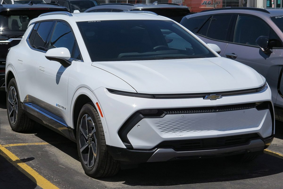 A white 2024 Chevrolet Equinox EV 2LT with a full-width light bar across its nose, parked on a dealer lot