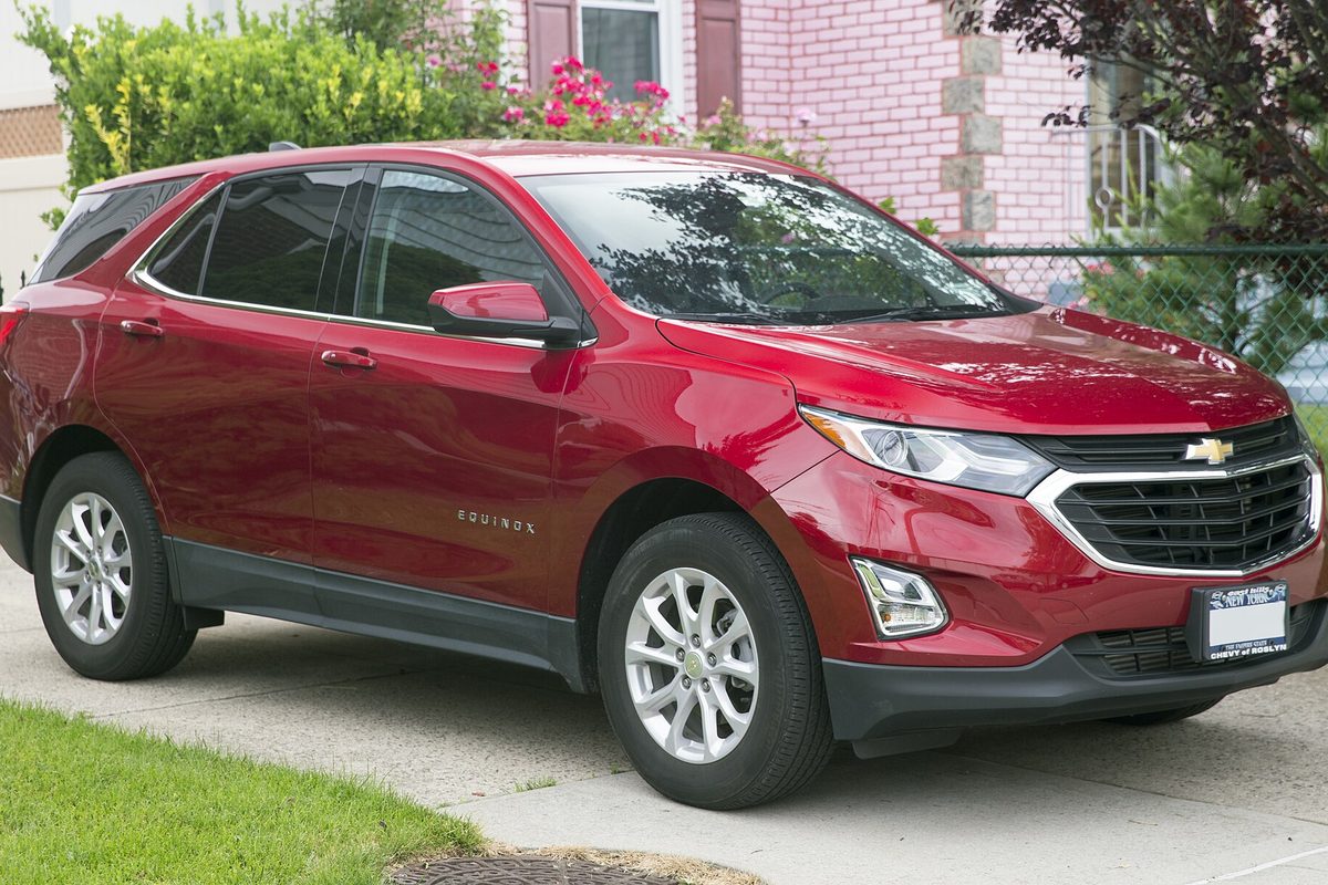 A red 2019 Chevrolet Equinox LT parked on a paved drive in front of a pink brick house and flowering shrubs