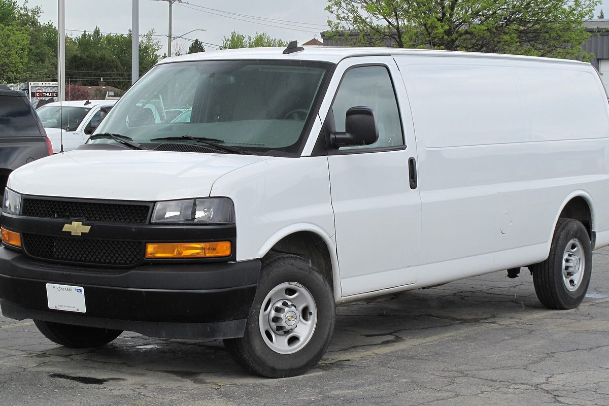 A white 2021 Chevrolet Express 2500 cargo van with plain steel wheels and an orange turn lamp, parked on a cracked asphalt lot