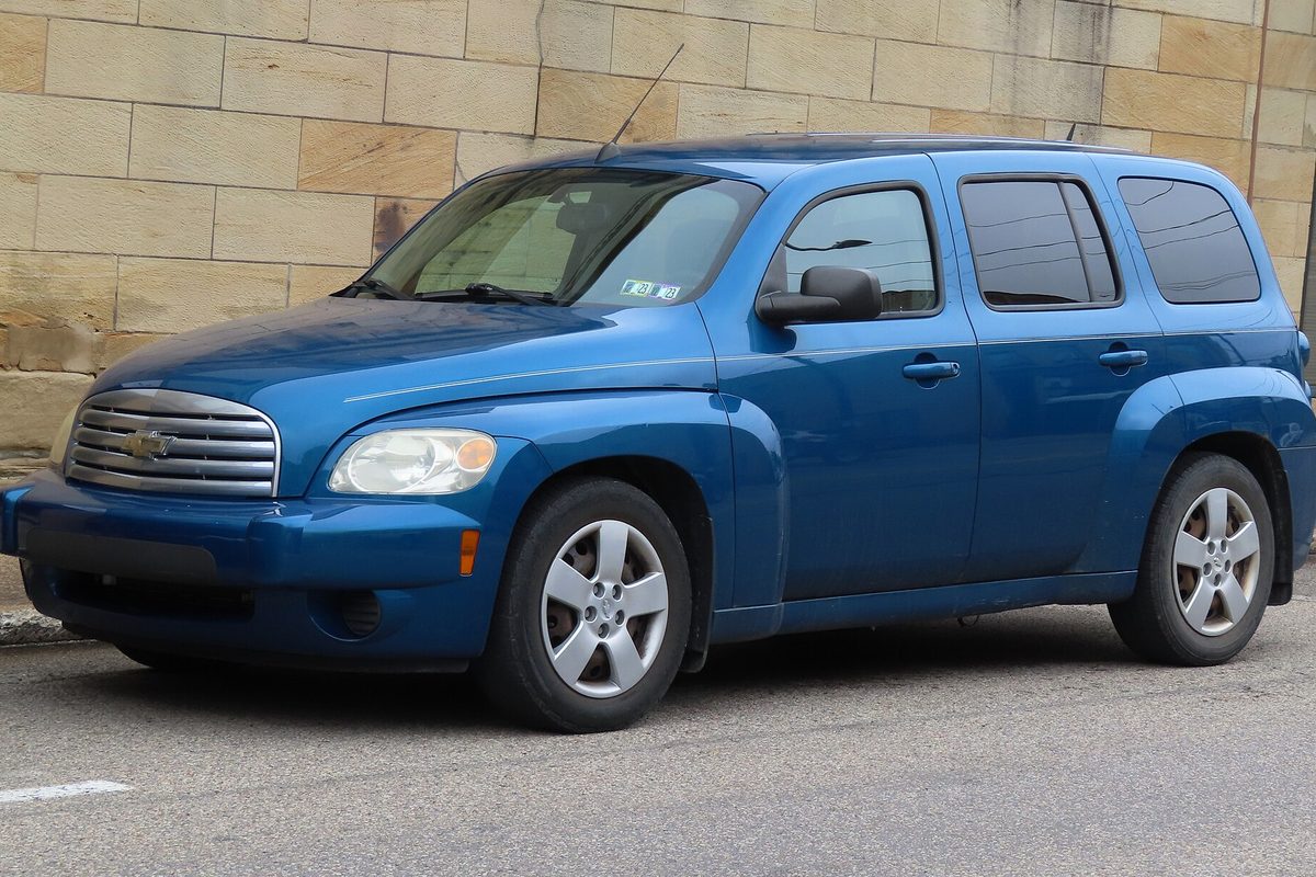A blue 2010 Chevrolet HHR LS parked at a street curb in front of a sandstone block wall