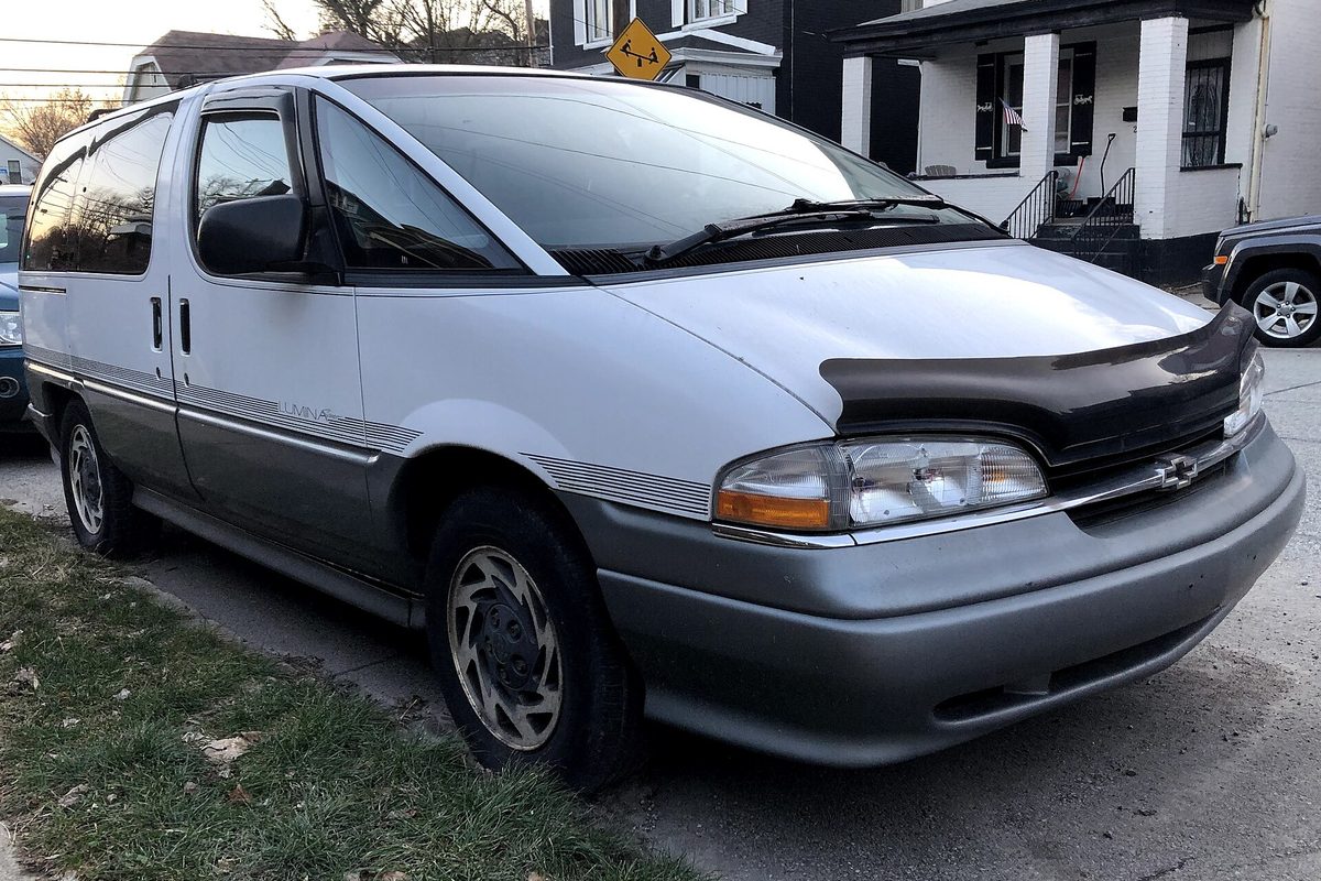 A white and gray 1996 Chevrolet Lumina APV Sport minivan with a black hood deflector, parked at the curb of a residential street