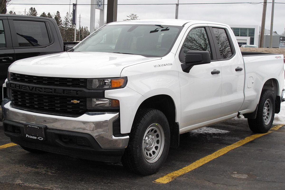 A white 2022 Chevrolet Silverado 1500 Work Truck double cab with black grille and steel wheels, parked in a lot with traces of snow