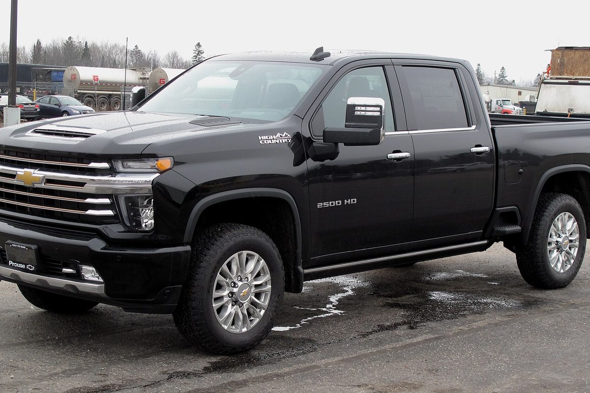 A black 2022 Chevrolet Silverado 2500HD High Country crew cab on wet, slushy pavement, with tanker trailers parked behind it