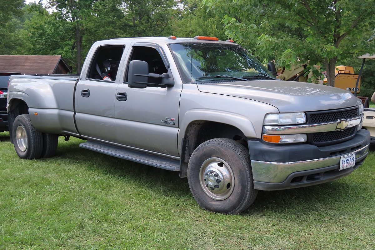 A pewter 2002 Chevrolet Silverado 3500 crew cab dually with amber roof lights, parked on grass under trees