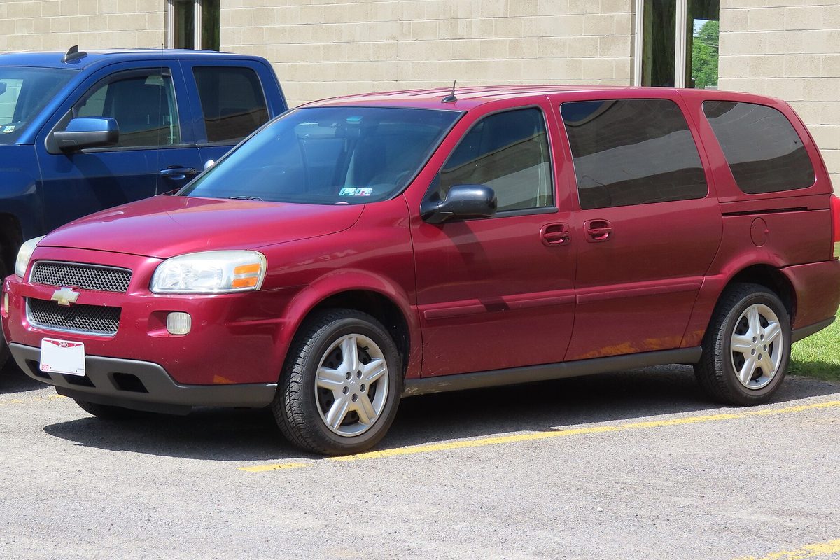 A red 2005 Chevrolet Uplander minivan with rust starting along the lower body, parked in a lot next to a blue pickup