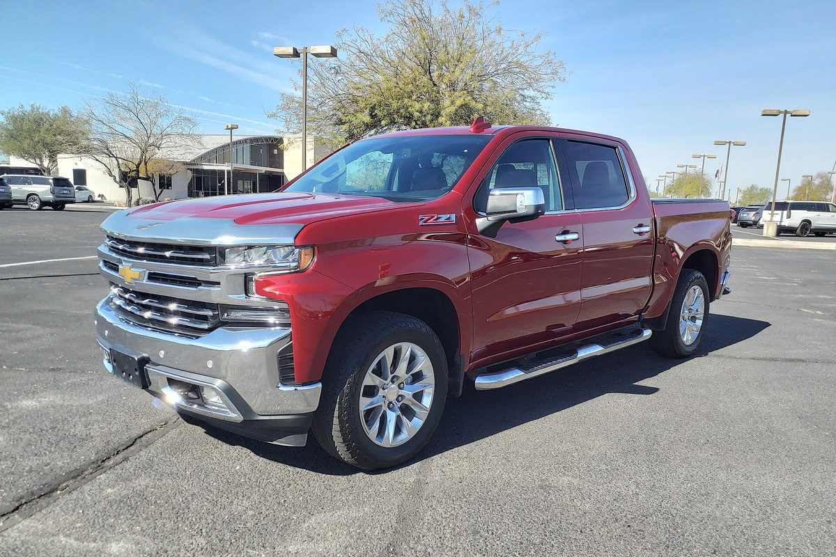 A red Chevrolet Silverado 1500 crew cab pickup with a chrome grille and a Z71 badge on the front fender, parked on a sunny asphalt lot with trees and a low building behind it