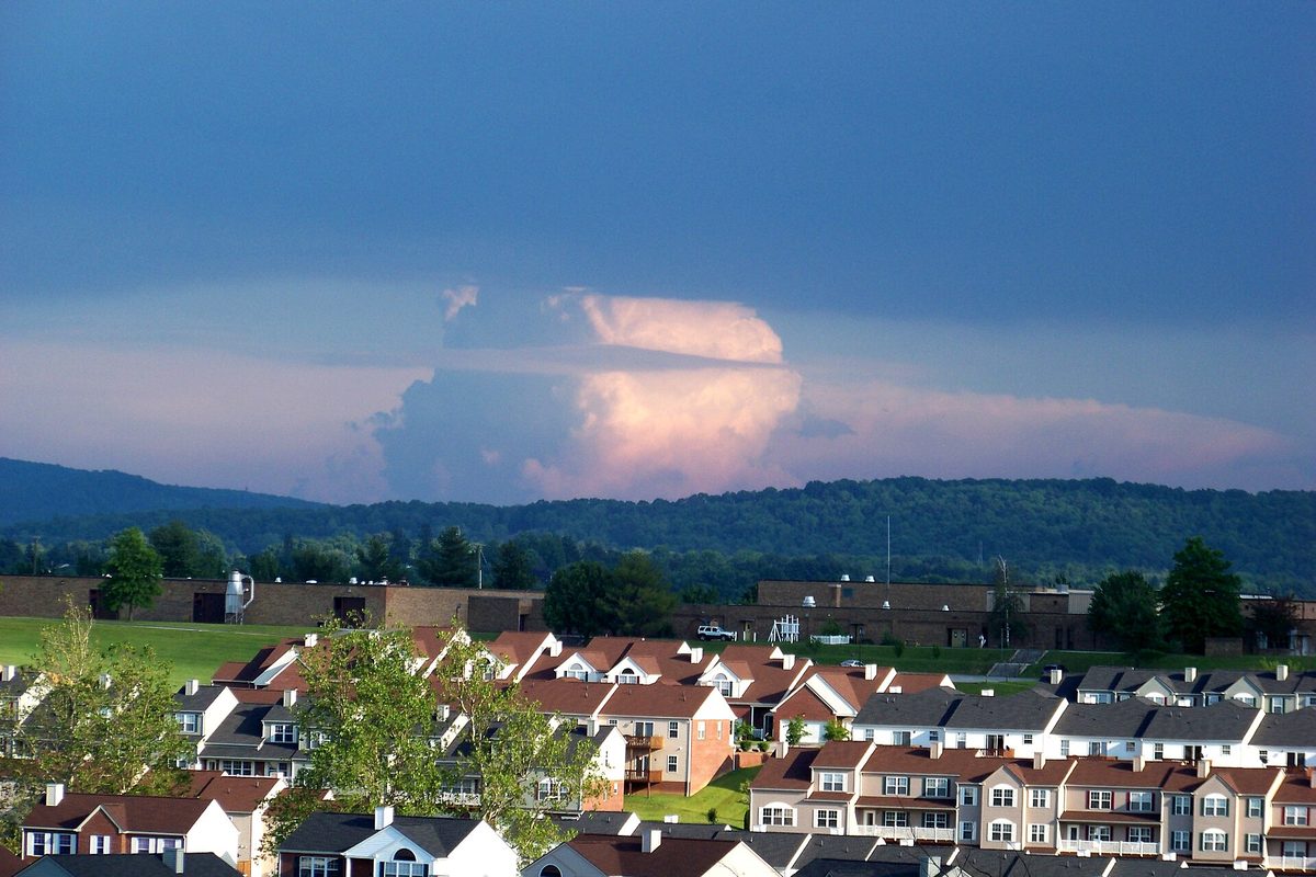 Rows of red-roofed townhouses below forested hills in Christiansburg, with a tall storm cloud glowing pink over the ridge toward Floyd