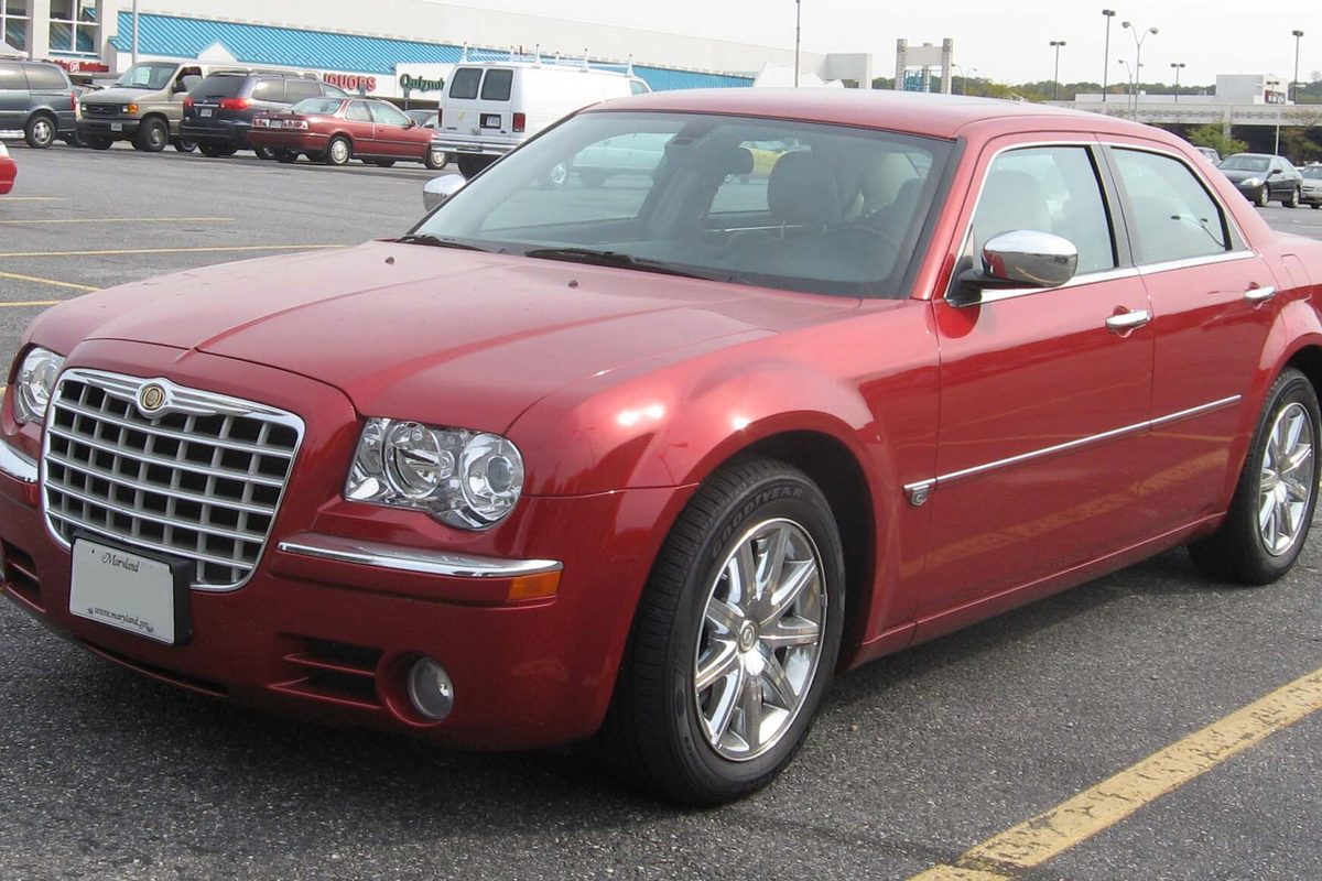 A red Chrysler 300C sedan with a chrome mesh grille, seen from the front left in a shopping center parking lot