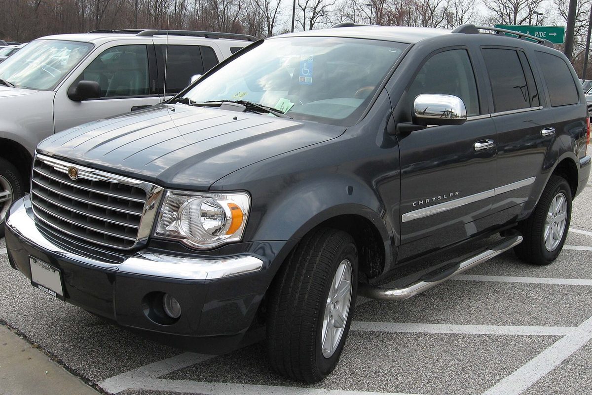 A dark gray Chrysler Aspen SUV with a chrome grille, chrome mirrors and running boards in a parking lot