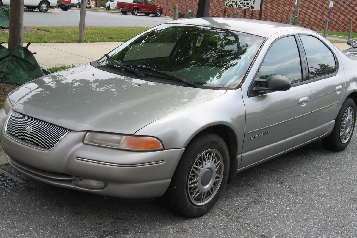 A silver 1995-1998 Chrysler Cirrus sedan parked at a curb beside a brick parking garage entrance