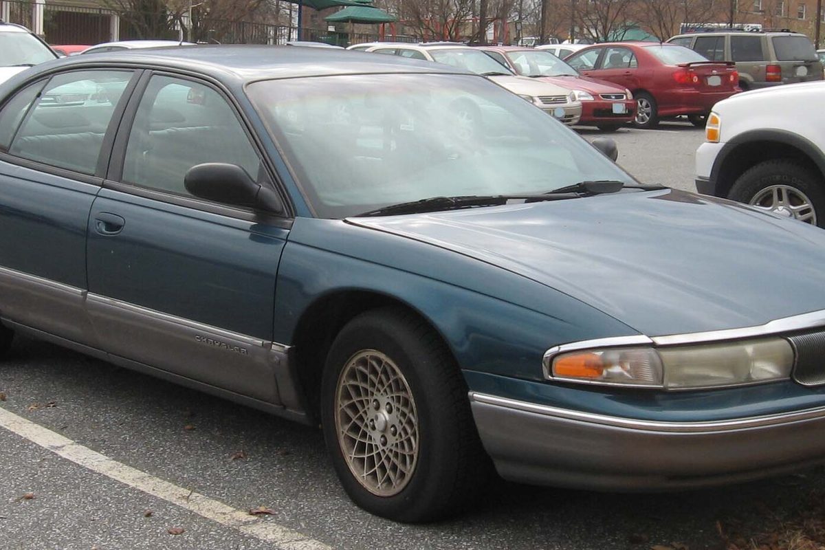 A teal 1994-1996 Chrysler New Yorker sedan with gray lower trim and lattice-pattern wheels in a parking lot