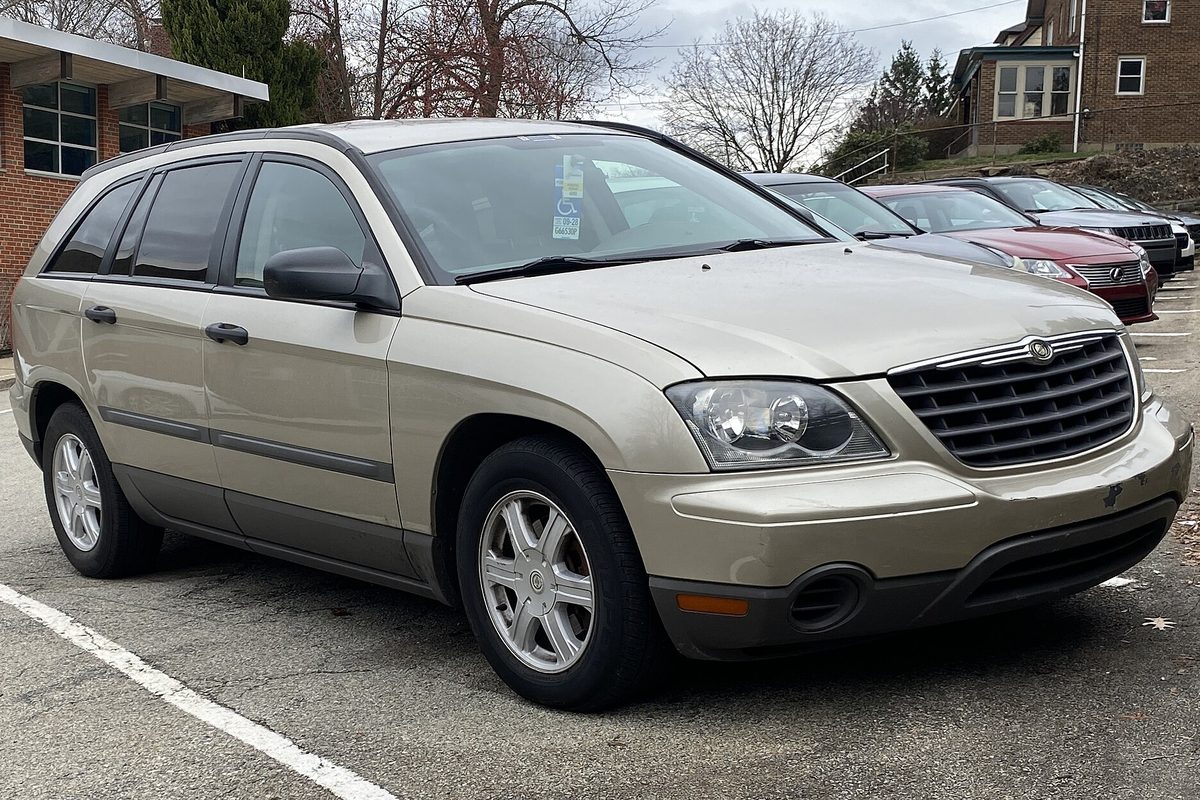 A light gold 2005 Chrysler Pacifica crossover, front right view, parked in a lot beside a brick building
