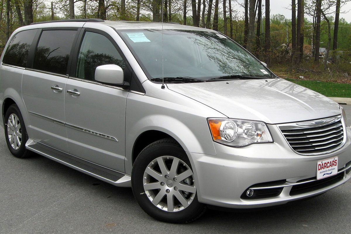 A silver 2011 Chrysler Town & Country minivan seen from the front right, parked on a road with bare trees behind it