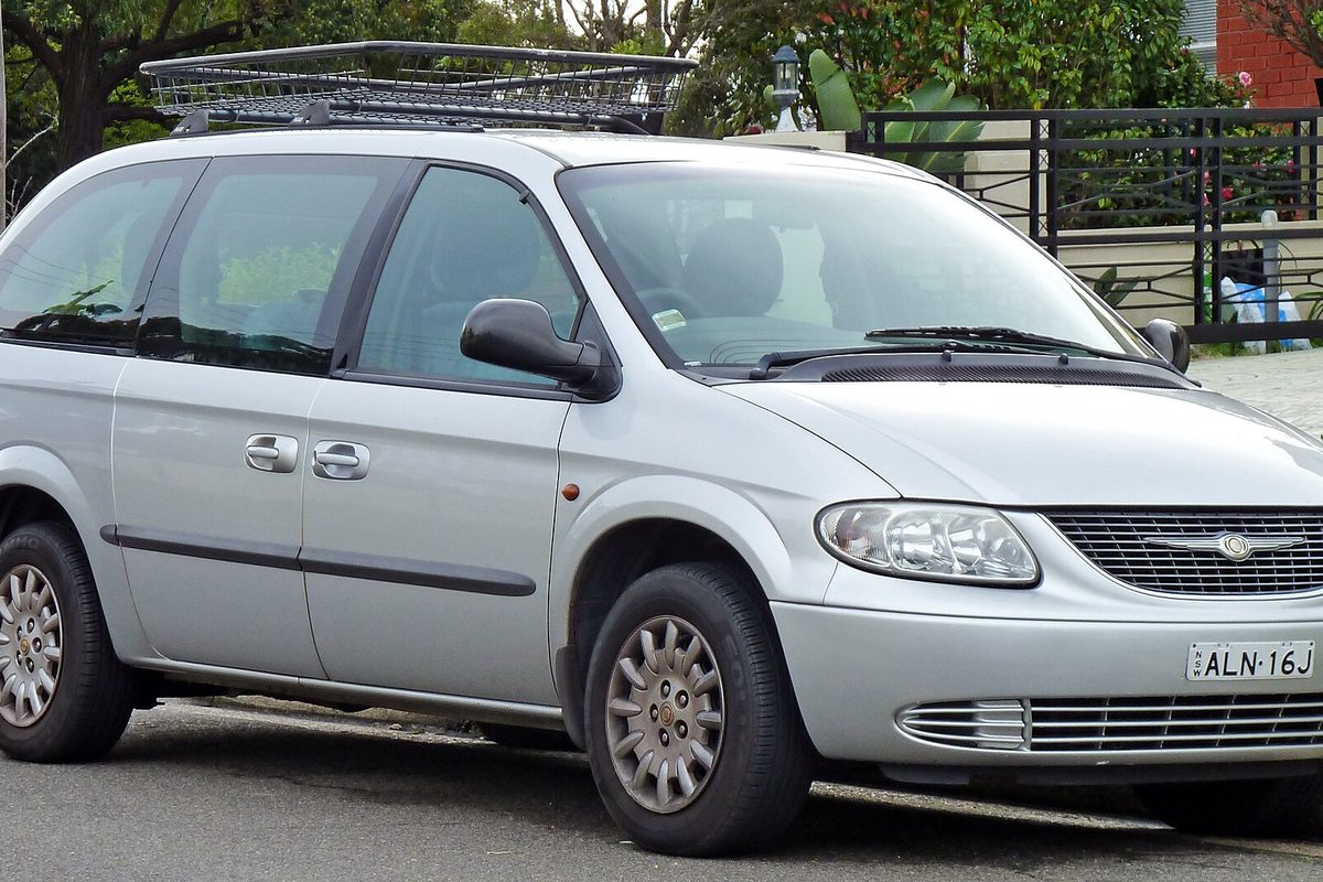 A silver Chrysler Grand Voyager minivan with a roof basket, parked at a curb on a residential street