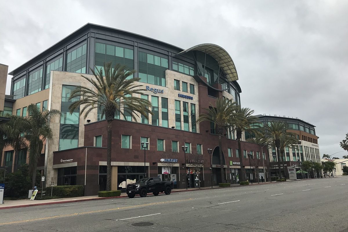 The Gateway office buildings in Chula Vista, glass and brick blocks with a curved roof, lined with palm trees under a gray sky, a dark pickup parked out front