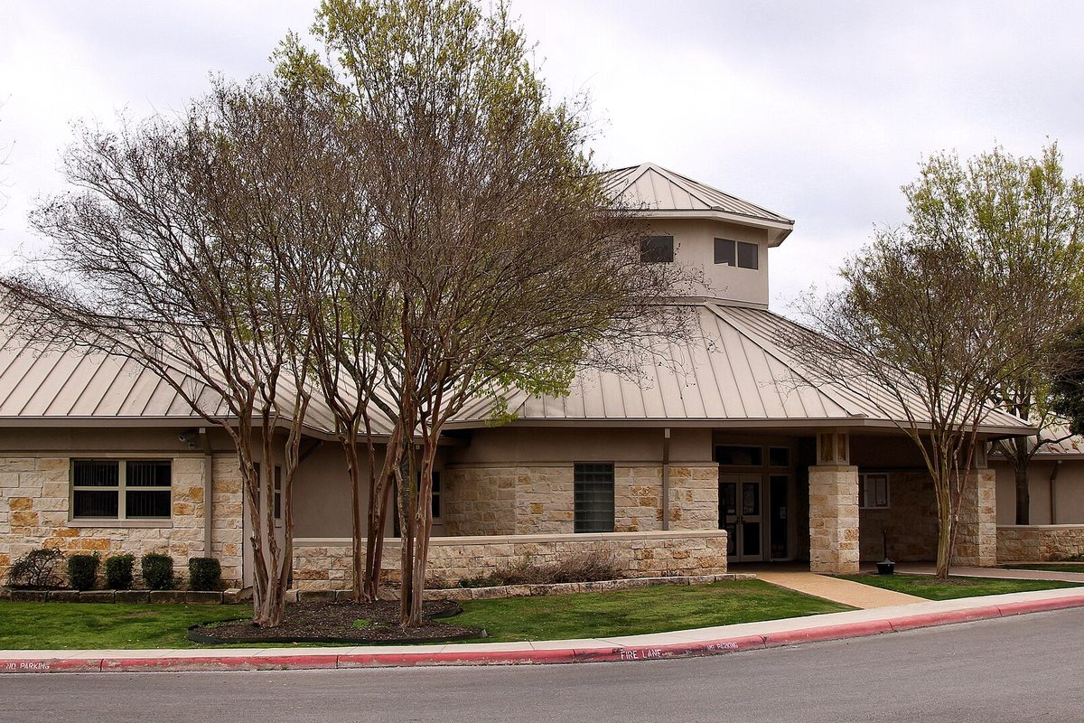 Cibolo City Hall, a low limestone building with a standing-seam metal roof, behind bare crape myrtle trees and a green lawn