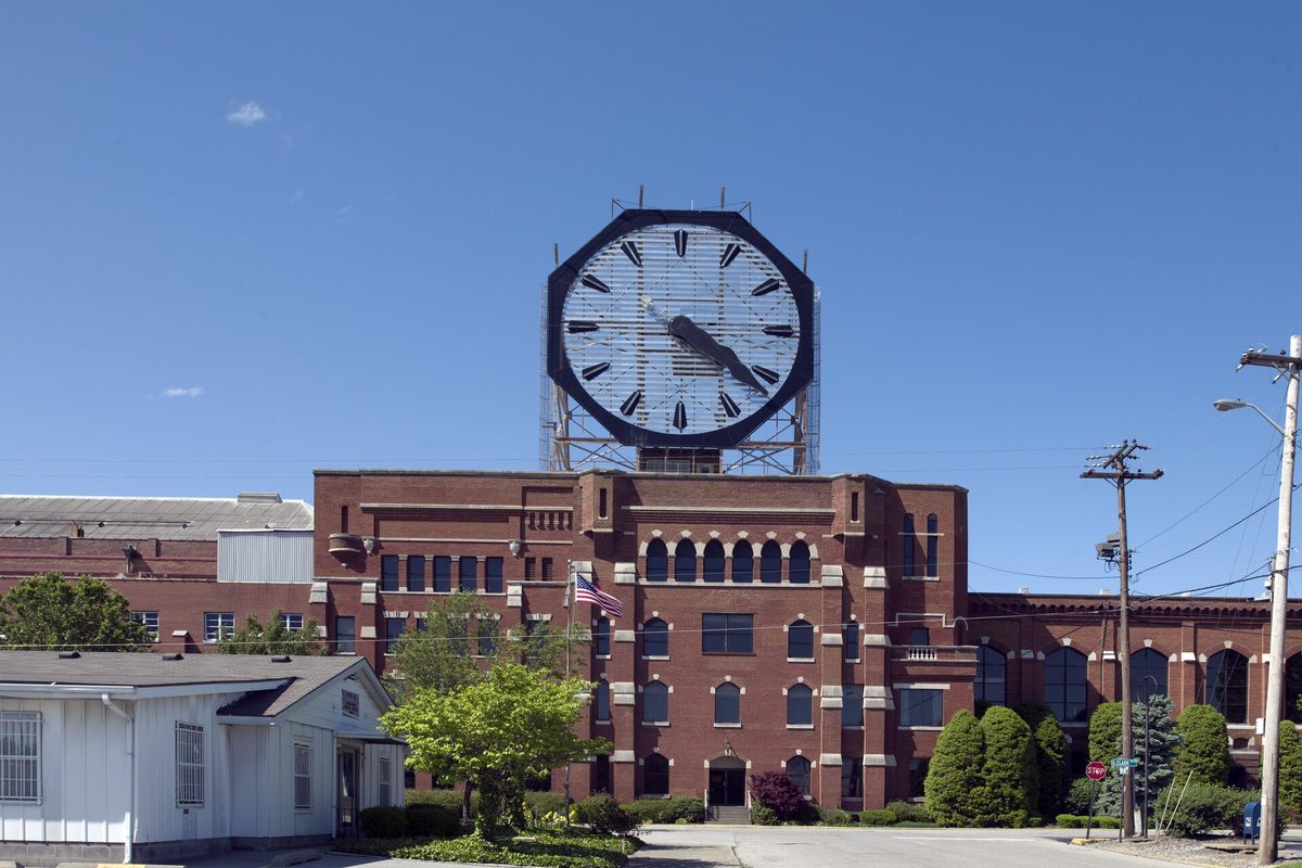The giant octagonal Colgate Clock standing on a steel frame above a red brick factory in Clarksville, under a clear blue sky
