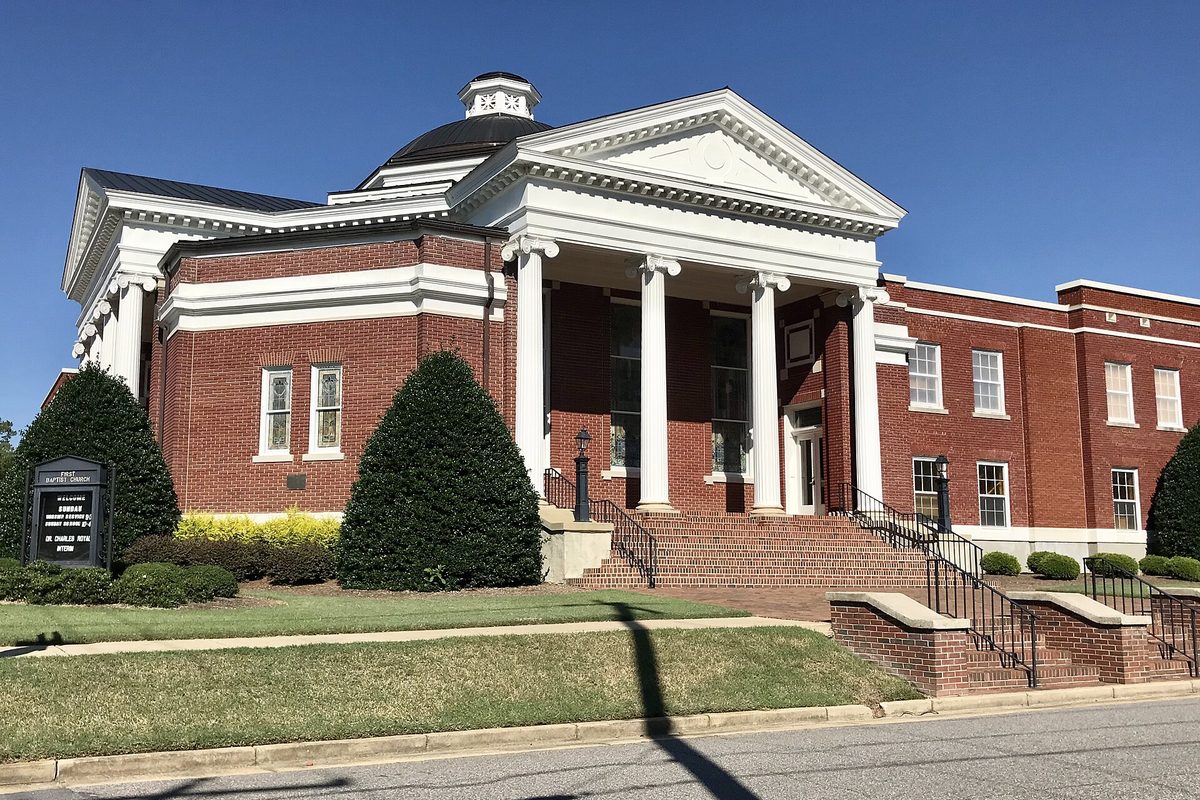 Clayton's First Baptist Church, a red-brick building with a white columned portico, a dome and wide front steps, behind a green lawn
