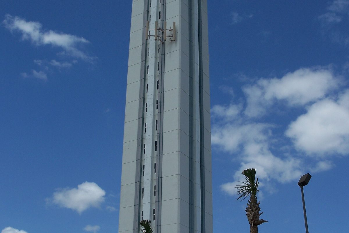 The tall white Citrus Tower in Clermont rising into a blue sky with scattered clouds, a palm tree and a lamp post below